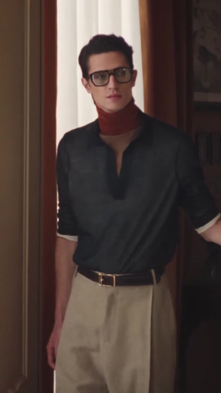 Man in black frames and a rust scarf standing in a doorway beside a pale curtain