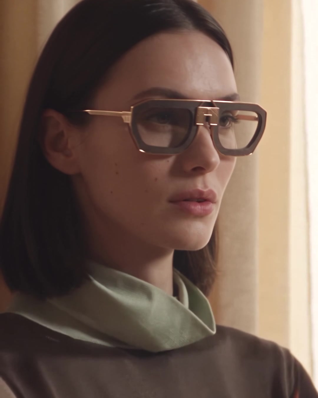 Woman in brown frames and a green scarf, close-up against a curtain
