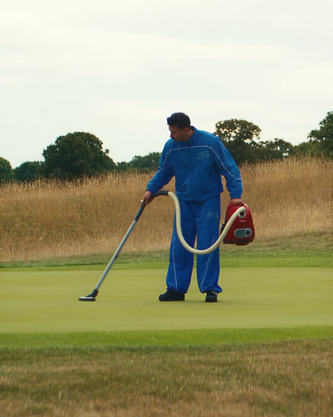 Man vacuuming a putting green with a red canister vacuum